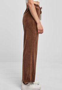 Brązowe, luźne spodnie z elastycznym paskiem w talii. Miękka tekstura, tapered design i gładkie wykończenie. W zestawie z białymi trampkami.
