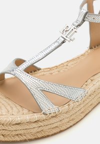 Silverfärgade metalliska sandaletter med remmar och en vävd juteplattform, med en texturerad ovandel och logotypdetalj. Platt sula design.