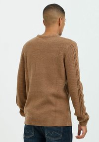 Suéter de punto marrón con un patrón texturizado y detalles de punto trenzado en las mangas, con un cuello redondo y puños acanalados.