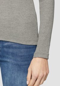 Haut gris à manches longues avec texture côtelée, en tissu naturel et ourlet arrondi, associé à un jean en denim bleu avec une légère décoloration.