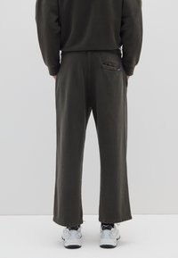 Dunkelgrüne Sweatpants mit lockerem Schnitt, elastischem Bund und Gesäßtasche, mit flachem Saum und weicher Textur. Kombiniert mit weißen Sneakers.