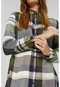 Chemise à boutons avec un motif à carreaux dans des nuances de vert, gris et blanc. Manches longues avec des poignets à boutons et un col mandarin.