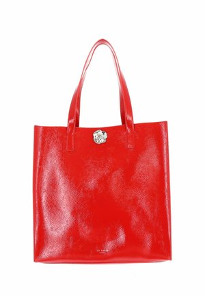Sac cabas en cuir rouge brillant avec deux anses et un petit emblème argenté en forme de fleur au centre avant.