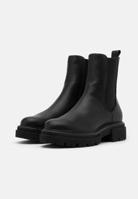 Botas Chelsea negras de cuero liso, con paneles laterales elásticos, una suela gruesa y texturizada, y lengüetas para ponerlas y quitarlas fácilmente.
