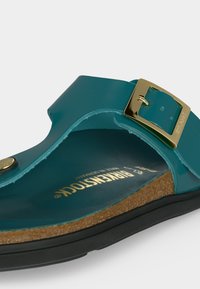 Σανδάλι Birkenstock σε τιρκουάζ χρώμα με φελλό στην σόλα, μαύρη εξωτερική σόλα και ρυθμιζόμενο χρυσό αγκράφα στον φαρδύ λουρί πάνω μέρος.