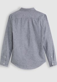Camicia a maniche lunghe in tessuto grigio chiaro con una finitura testurizzata. Presenta un colletto, polsini con bottoni e un orlo curvo. Dettaglio della piega sul retro visibile.