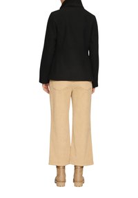 Schwarze Wolle-Mischung Jacke mit hohem Rippenkragen, kombiniert mit weiten beigen Cordhosen. Tanfarbene Stiefeletten mit kräftigen Sohlen.