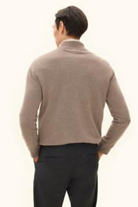 Maglione in lana marrone con colletto alto e design aderente. Presenta polsini a coste e una texture liscia, abbinato a pantaloni scuri.