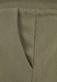 Närbild av olivgrön stickad tyg som visar en sidoficka och detaljer med ribbat midjeband.