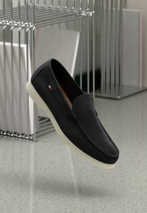 Black slip-on shoe made of leather, featuring a white rubber sole and subtle accent detailing. Smooth texture and classic design.