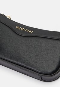Čierna kožená večerná kabelka s zlatým logom "VALENTINO", elegantný dizajn, textúrovaný povrch a zips so zaobleným tvarom.