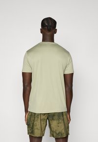 Lys grønn t-skjorte med korte ermer og rund hals, i kombinasjon med shorts med camouflagemønster, som viser en glatt tekstur og atletisk passform.