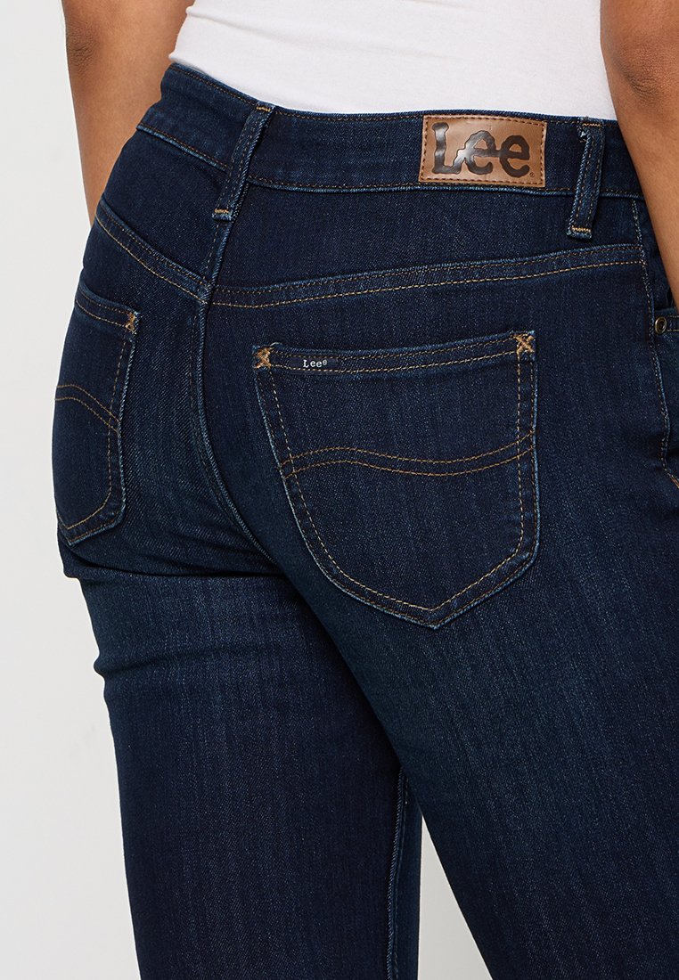 Jeans in denim blu scuro con etichetta in pelle marrone Lee, tasche cucite e design aderente con leggere sfumature e texture.