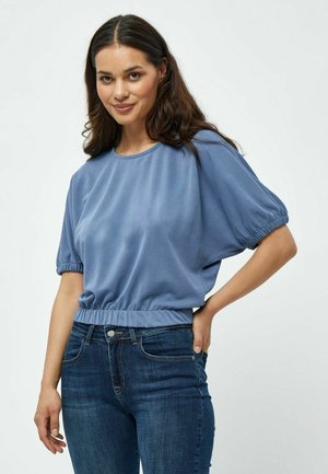 Lichtblauw, kortmouwtop met een ruime pasvorm en een verzamelde elastische tailleband, gecombineerd met donkerblauwe skinny jeans. Glad stofoppervlak.