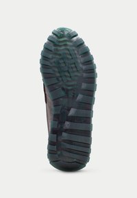 Suola nera da scarpa con profonde scanalature e righe per una migliore aderenza. Gomma testurizzata con accenti verdi e dettagli di branding. Costruzione robusta.
