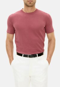 T-shirt a maniche corte, aderente, con collo rotondo di colore rosa polveroso, realizzato in tessuto a maglia morbida, abbinato a pantaloni bianchi e una cintura nera.