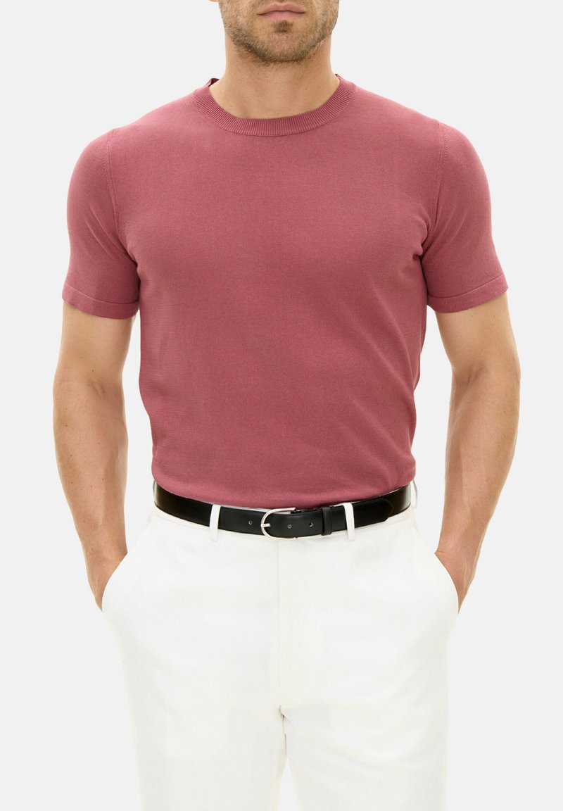 T-shirt a maniche corte, aderente, con collo rotondo di colore rosa polveroso, realizzato in tessuto a maglia morbida, abbinato a pantaloni bianchi e una cintura nera.