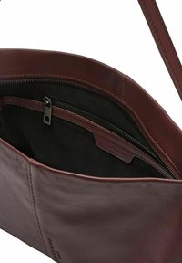 Wnętrze bordowej skórzanej torebki z kieszenią na zamek i czarną podszewką. Charakteryzuje się gładką fakturą oraz skórzaną metką z logo marki.