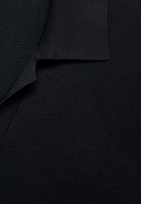 Tejido de punto negro con una superficie texturizada. Presenta un cuello doblado con un borde suave, destacando un tono profundo y un patrón uniforme.