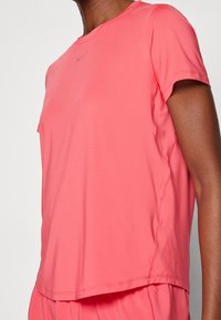 Camiseta atlética de manga corta en un coral vibrante. Fabricada con un tejido ligero de textura suave y detalle del logo reflectante cerca del escote.