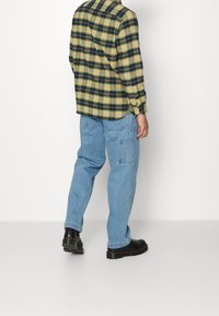 Rutig flanellskjorta i gult och grönt, kombinerad med ljusblå cargo-byxor. Svarta skor med en texturerad sula.