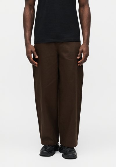 Pantalones marrones de pierna ancha hechos de tela suave, con una textura lisa y un ajuste relajado, combinados con zapatillas negras.