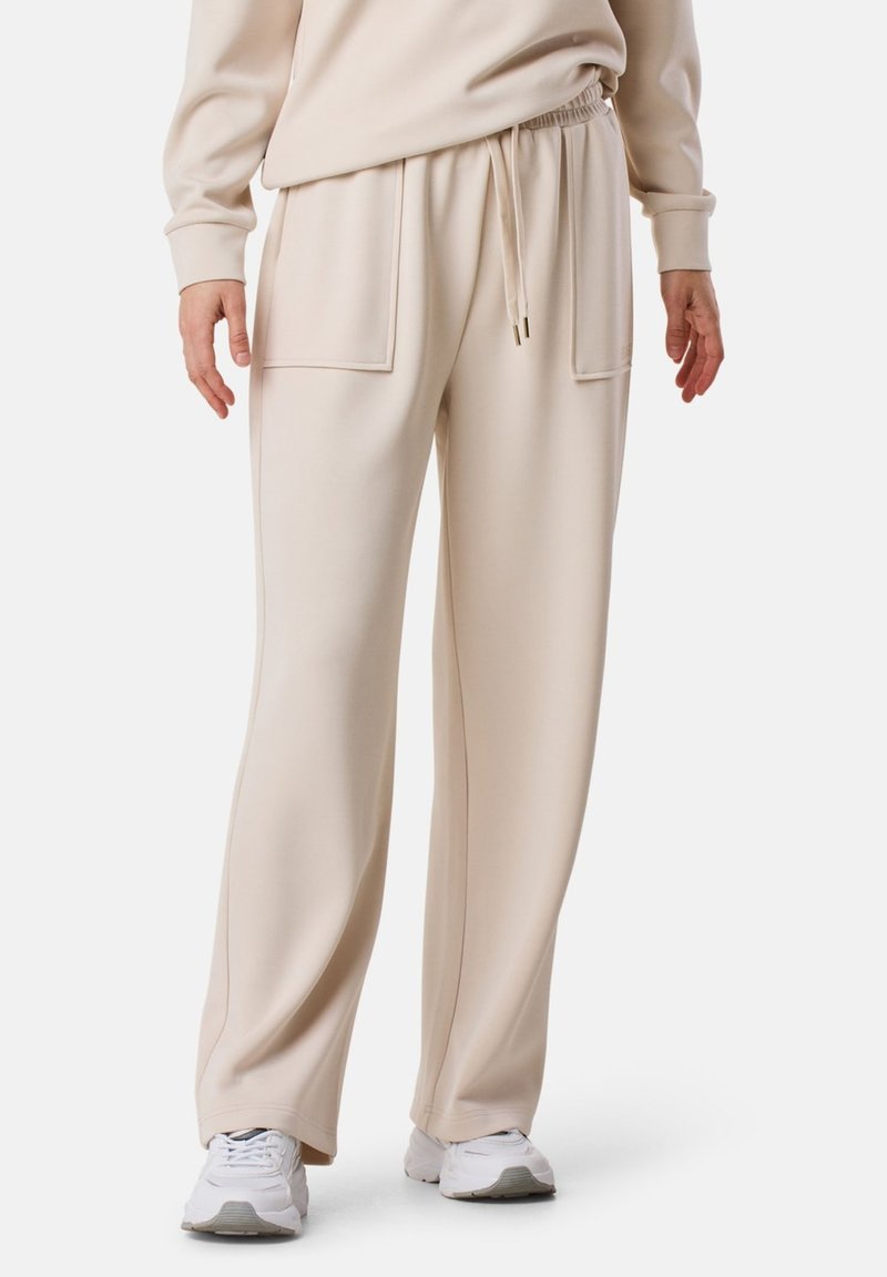 Beige elastische taillebandbroeken met zijzakken, relaxte pasvorm en gladde textuur. Gemaakt met witte sneakers.