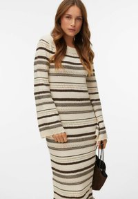 Kräm- och brunsrandig tröjklänning med långa ärmar, ribbad textur och böljande muddar, med en avslappnad passform och stickade detaljer.
