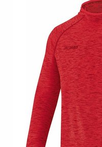 Maglietta rossa a maniche lunghe realizzata in materiale texturizzato. Caratterizzata da un colletto alto e maniche raglan. Logo JAKO stampato sul davanti.