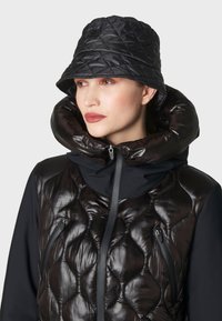 Giacca nera gonfiabile con texture trapuntata, tasca con zip, colletto alto e cappuccio, abbinata a un berretto a secchiello nero coordinato.
