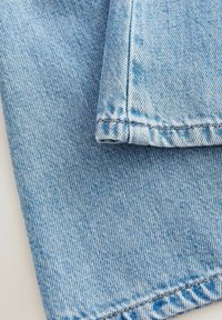 Lichtblauwe denimstof met een visgraatpatroon, die een gladde textuur toont en contrasterende oranje stiksels langs de randen.