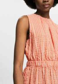 Robe sans manches en orange clair avec des rayures verticales blanches, présentant une taille froncée et des plis subtils au niveau du col. Tissu texturé.