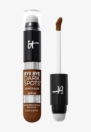 Tuba korektora i serum oznaczona jako "Bye Bye Dark Spots" z podwójną szczoteczką aplikacyjną i pędzelkiem, pokazująca średnio brązowy odcień produktu.