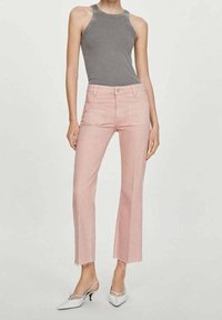 Jeans de color rosa claro con dobladillo deshilachado, diseño de cintura alta y dos bolsillos frontales, combinados con una blusa sin mangas gris y zapatos blancos de punta.