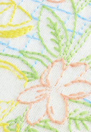 Weißer Stoff mit detaillierter floralem Stickerei in Pastellfarben, mit rosa Blütenblättern, gelben Blättern und grünen Stängeln, vor einem blauen Karomuster.