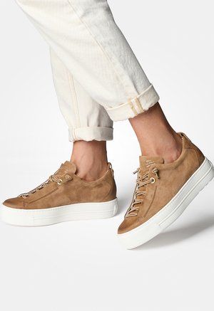 Baskets en suède marron avec une finition texturée, semelle en caoutchouc blanc et détails de lacets contrastés. Design épuré et arrondi avec des accents minimaux.