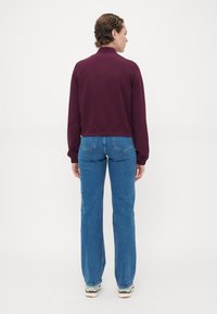 Maroon cropped jacket with long sleeves and ribbed hem, paired with light blue high-waisted jeans featuring a classic five-pocket design.