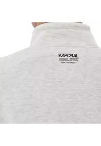 Lichtgrijze sweatshirt met een zachte textuur. De achterkant heeft een zwart merketiket met de tekst "KAPORAL REBEL SPIRIT NON CONFORMIST".