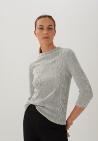 Schwarz-weißer gemusterter Oberteil mit Dreiviertelärmeln, rundem Ausschnitt und strukturiertem Stoff, getragen mit schwarzen Hosen.