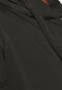 Svart puffjacka med en slät, blank yta. Har en hög krage och en lätt glans, med synliga sömmar längs sömmarna.