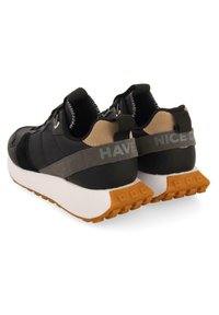 Svarta sportskor med en strukturerad ovandel, grå accenter och en gummiyttersula. Har ett "HA EN BRA DAG"-bälte på hälen.