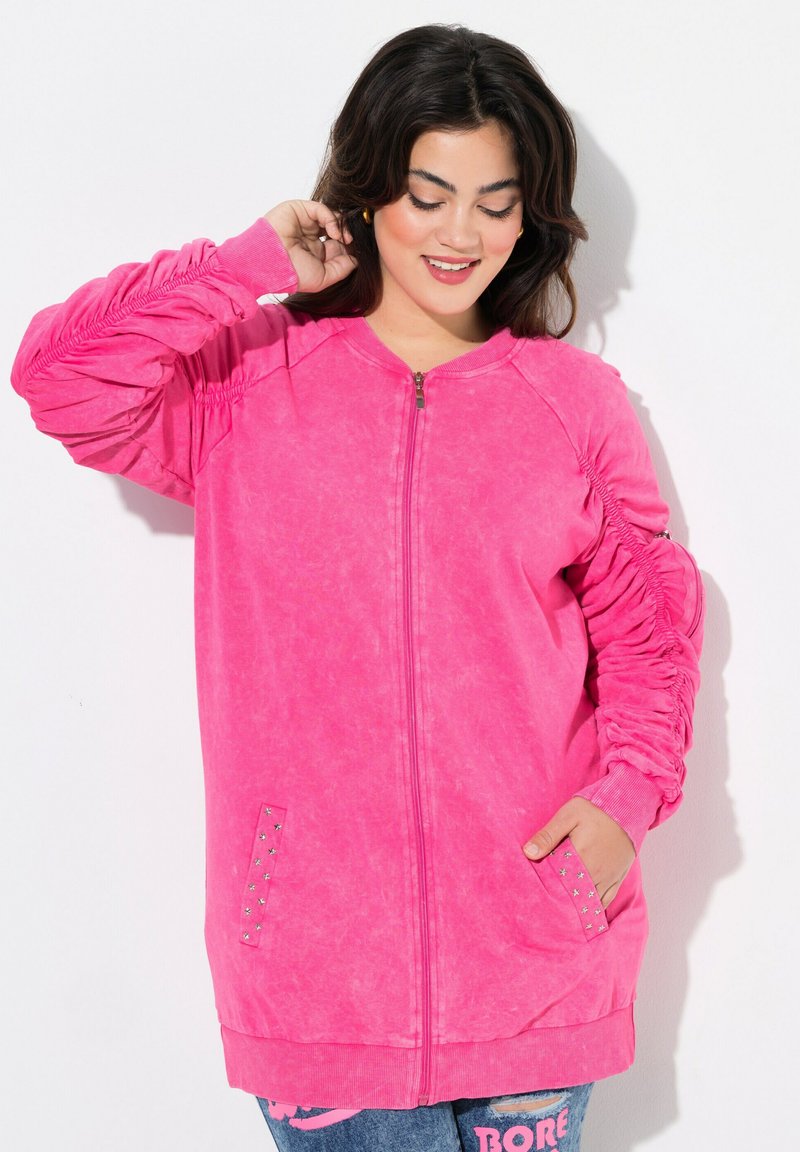 Sudadera rosa con cremallera y mangas texturizadas, puños acanalados y detalles de tachuelas en los bolsillos. Tejido suave y ligero.