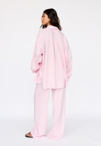 Roze, oversized shirt met een zachte textuur en lange mouwen, gecombineerd met bijpassende loszittende broek, beide met een relaxte pasvorm.