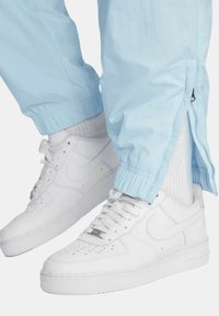 Ljust blå joggerbyxor med elastiska muddar och dragkedjor på sidorna, ihopparade med vita lädersneakers Nike Air Force 1 och vita strumpor.