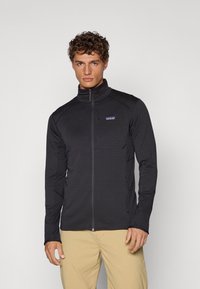Black zip-up jacket featuring a textured surface, high collar, and side pockets, made from lightweight and breathable material.