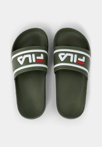 Olivgrön slidesandal med breda gummiband som har vit och röd FILA-logotyp. Texturerad fotbädd för grepp. Platt sula.