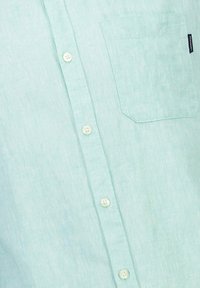 Vaaleansininen pellavapaita, jossa on napillinen etuosa, yksi rintatasku ja vaaleat napit. Pehmeä tekstuuri ja rento muotoilu.