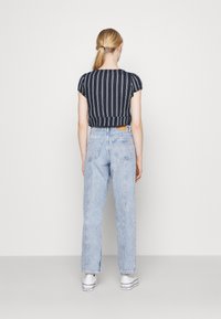 Randig, kort topp i marinblått och vitt, ihop med ljusblå, högmidjade jeans och vita sneakers. Synliga bakfickor på jeansen.