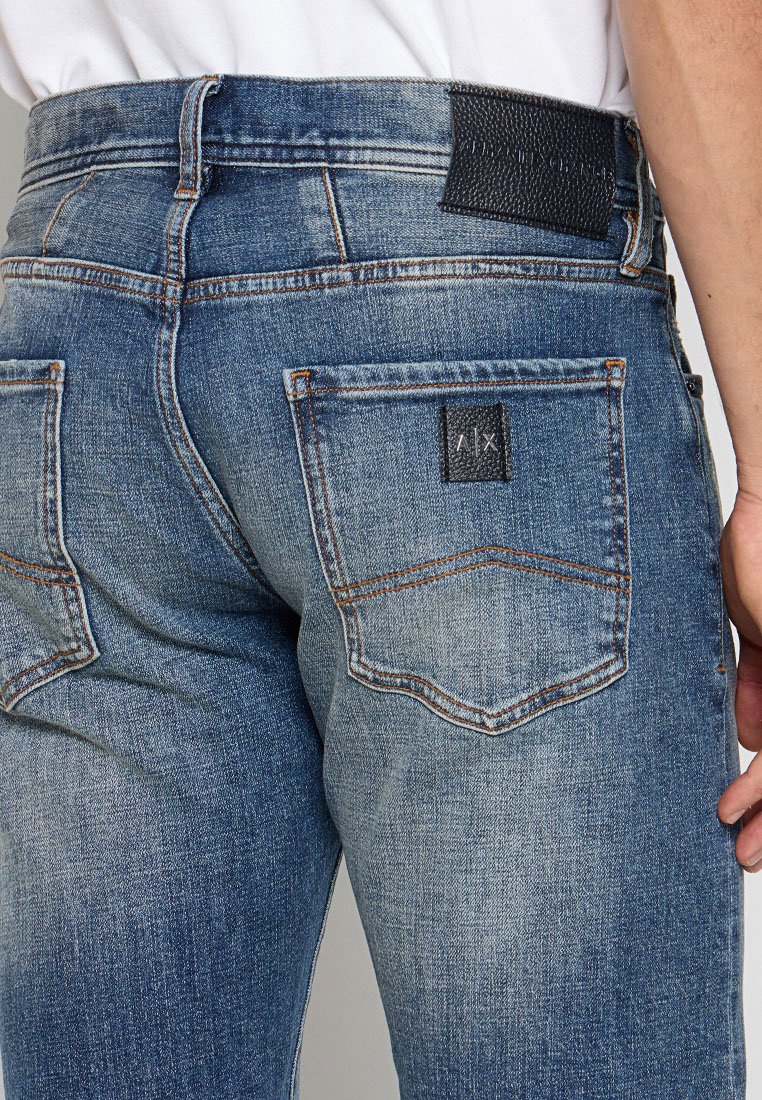 Jeans in denim blu con una toppa scura in vita, due tasche posteriori con dettagli cuciti e una finitura sbiadita per un effetto texture.