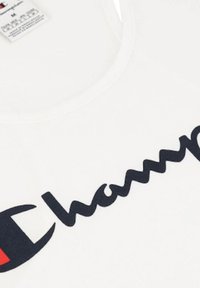 Hvid tanktop med et stort sort "Champion" logo og rød accent inden for et sort emblem. Glat tekstur og rund halsdesign.